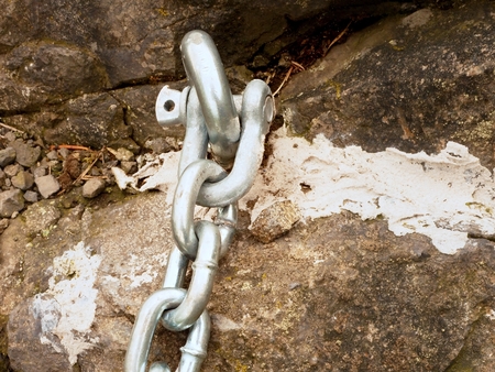 Detail of chain and steel bolt anchor eye in sandstone rock. The end knot of steel chain. Climbers path via ferrata. Iron chain fixed in block.の写真素材