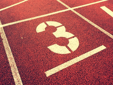 Number three. White track number on red rubber racetrack, texture of running racetracks in small...