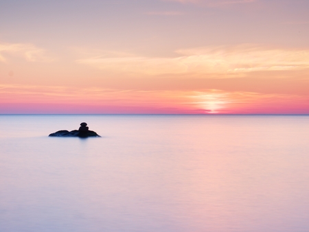 Romantic morning at sea. Big boulders sticking out from smooth wavy sea. Pink horizon with first hot sun rays.の写真素材