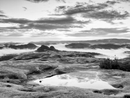 Black and white photo. Misty daybreak in a beautiful hills. Peaks of hills are sticking out from...