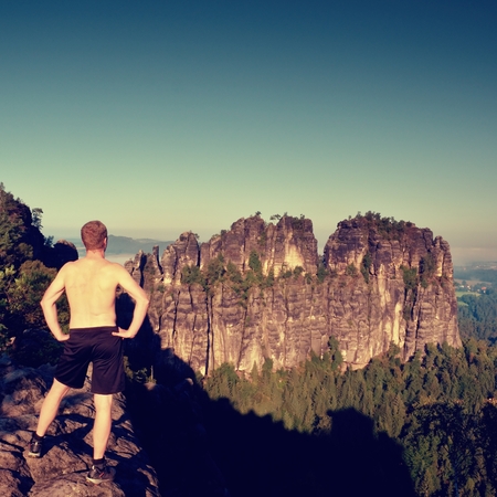 Naked man in black pants only at the top of the rock side.  Sharp sandstone cliffs above deep valley. Popular climbers resort.の写真素材