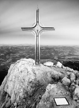 Cross raised  at mountain summit  in Alps. Sharp peak, daybreak Sun in sky. Steel crucifix in memory of victims of mountains. Vivid photo.の写真素材