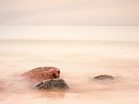 Long exposure of sea and big boulders sticking up from water within twilight time. Pink sunset at rocky coast of Balsitc  sea.の写真素材