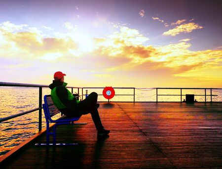 Man hiker on mole at sea. Tourist on wharf looking ower sea to horizon. Sunny clear blue sky, smooth water levelの写真素材