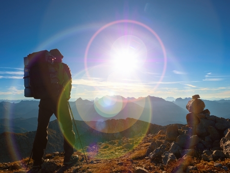 Lens flare light, strong defect. Man hiker with rucksack walk  on rocky peak. Tourist  walking over rocky summit to Sun. Beautiful moment the miracle of nature.の写真素材