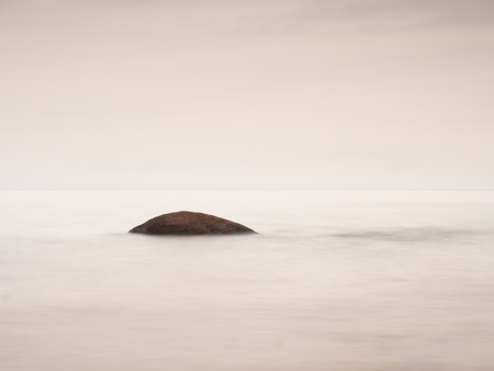 Romantic sea. Boulder stick out from smooth wavy sea. Pink horizon touch water level.の写真素材
