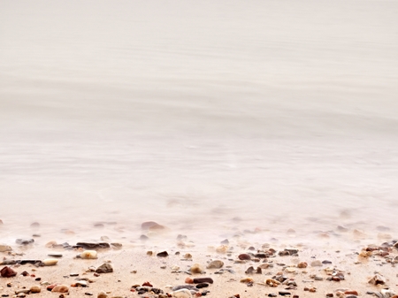 Pebbles on sandy beach against foamy sea water. Natural romantic offshore background, sunset colors  of oceannの写真素材
