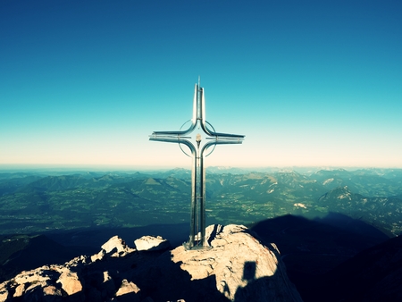 Cross with semi-precious stone raised  at mountain summit  in Alps. Sharp peak. Daybreak Sun in sky. Steel crucifix in memory of victims of mountains. Vivid photo.の写真素材