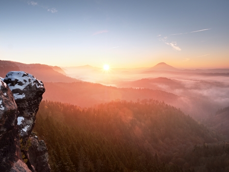 Cocks covered with fresh powder snow, misty valley. Stony rock peak increased from foggy valley. Winter misty sunrise in a beautiful rocks empire.の写真素材