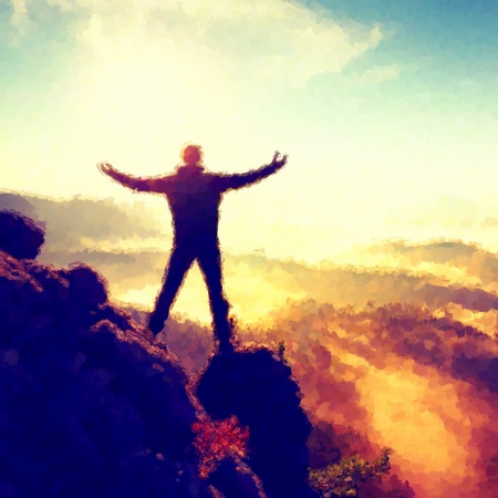 Watercolor paint effect.  Happy hiker with raised hands in air stand on rock above forest. View over misty and foggy morning valley to Sun.の写真素材