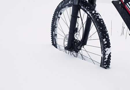 The front wheel of mountain bike stay in powder snow. Lost path under deep snowdrift. Snow flakes melting on dark off road tyre.  Winter weather in the field.の写真素材