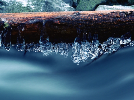 Icy branches above  chilling stream. Bright reflections in icicles, blur white foam on water level. Icy artの写真素材