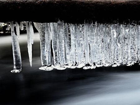 Icy branches above  chilling stream. Bright reflections in icicles, blur white foam on water level. Icy artの写真素材