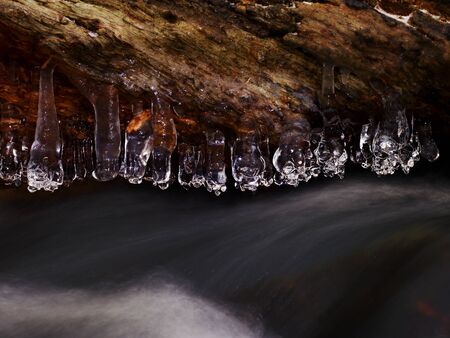 Icy branches above  winter creek. Bright reflections in icicles, blur white foam on water level. Icy artの写真素材