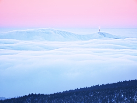 Far mountain peak with observatory above creamy mist. Shinning lights on antenna. Wavy fog in vally bellow, inverse winter weather.の写真素材
