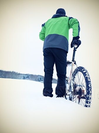 Man with mountain bike stay in powder snow. Lost path  in deep snowdrift. Rear wheel detail. Snow flakes melting on dark off road tyre.  Winter weather in the field.の写真素材