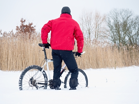 Sportsman with mountain bike lost in snow. Lost path  in deep snowdrift.  Snow flakes melting on dark off road tyre.  Winter weather in the field.の写真素材