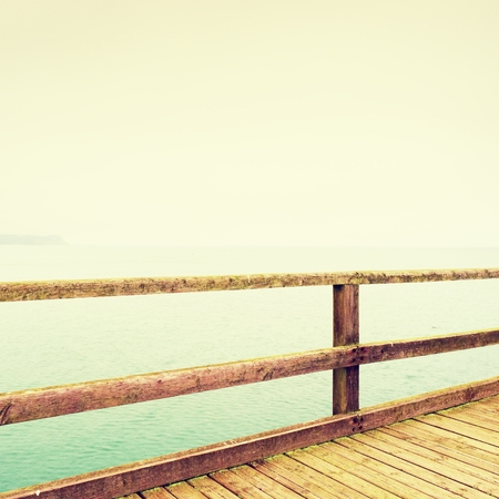 Empty catwalk. Autumn misty morning on wooden pier above sea. Depression, dark atmosphere. Touristic mole, wet wooden floor above sea.の写真素材