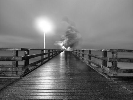 Man Ghost Walk in autumn mist on wooden pier above sea. Depression, dark atmosphere. Touristic mole, wet wooden floor above sea.の写真素材