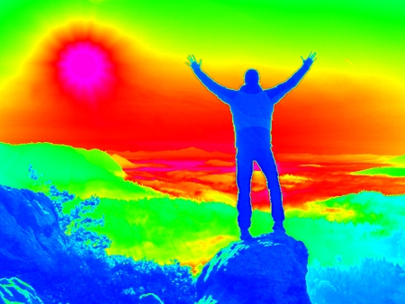 Man on rock. Fantastic infrared scan. Tourist on the rocky peak. Daybreak in mountains, heavy mist in deep valley in colors of ultra violet measurementの写真素材