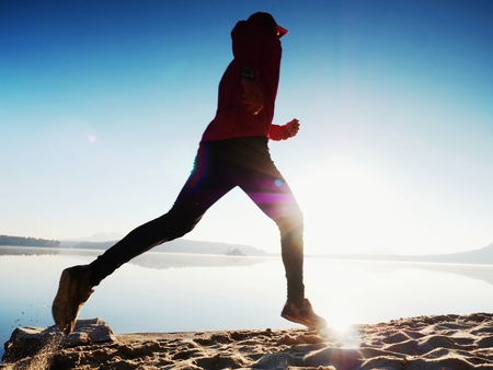 Slim young fitness man runner on beach, tropical trail runner.  Cheerful sportsman run on beach among the water, personal  event. Sunrise hot sun at horizon in backgroundの写真素材