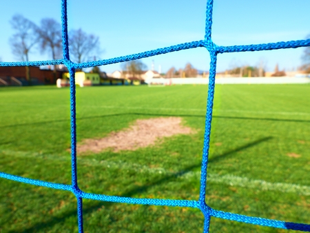 Detail of yellow blue crossed soccer nets, soccer football in goal net with grass on outdoor playground in the background.の写真素材