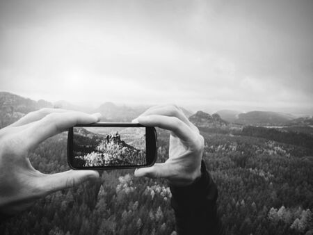 Man takes photos with phone on rock empire. Dreamy fogy mountains, spring orange pink misty sunrise...