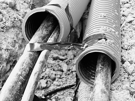 Excavation of trench with black cables in protective HDPE tube. Lines of metallic and fiber optic...