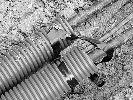 Excavation of trench with black cables in protective HDPE tube. Lines of metallic and fiber optic...