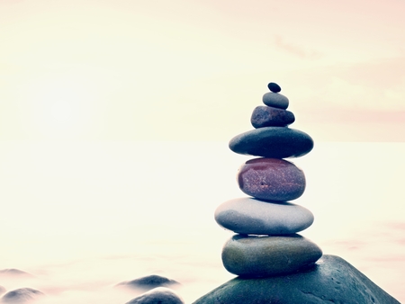 Stacked rounded stones at sea. Small polished pebbles stack on dark wet rock,  blue smooth water of ocean in backgroundの写真素材