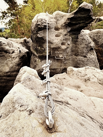 Iron twisted rope stretched between rocks in climbers patch via ferrata.  Rope fixed in block by screws snap hooks. Detail of rope end anchored into sandstone rockの写真素材