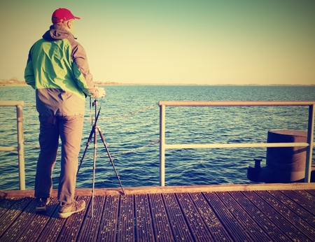 Man, photographer taking photos at the lake at sunset. Windless at sea wooden pier. Hobby photographer on vacation.の写真素材