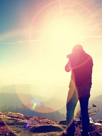 Tall Man is taking photo camera on the mirror neck. Snowy rocky peak of mountain. Professional photographer Takes photos with mirror camera on snowy peak of rock.の写真素材