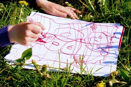 Close up view of child's hand drawing colorful ornaments on paper. Notebook in fresh grass of meadow.の写真素材