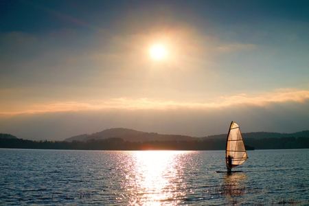 Windsurfer leans back into breeze Shot with gentle filter. Strong sun makes reflections in mirror of water level.の写真素材