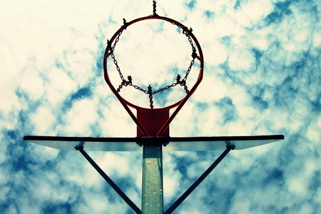 Old neglect basketball backboard with rusty hoop above street court. Blue cloudy sky in bckground.の写真素材