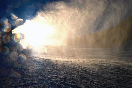 Snowmaking on slope. Skier near a snow cannon making fresch powder snow. Mountain ski resort and...