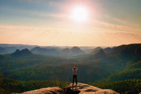 Tourist takes photos with smart phone on rocky empire. Fogy landscape, spring orange pink misty sunrise in a beautiful valley of Saxony Switzerland park.の写真素材
