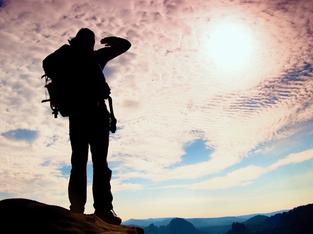 Tourist with big backpack stand on rocky view point and watching into deep misty valley bellow.の写真素材