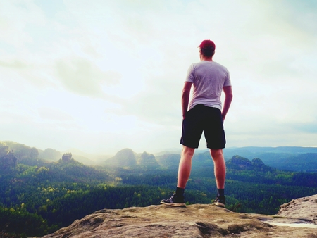 Man in t-shirt and pants. Tourist on mountain peak looking into misty landscape.の写真素材