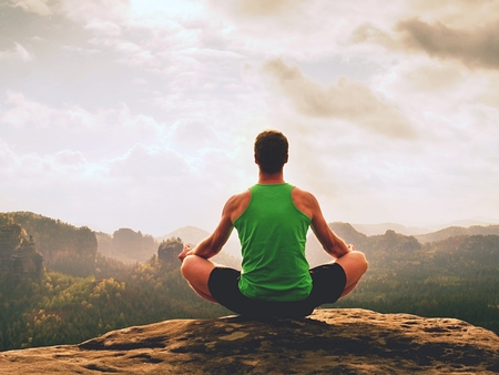 Alone man doing yoga pose on the rocks peak in misty morning. Middle-aged man practicing yoga and meditation in mountains during a luxury weather evening.の写真素材