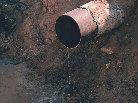 Rusty Old Iron Pipe With Clear Water Flowing From It. Waste water drain pipe in clayの写真素材