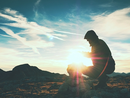 Alone hiker man on the top of the Alpine mountain building pyrmid from pebbles. Mans hand hold the last stone for the pyramid.  Stones on Alps mountain gravel summit.の写真素材