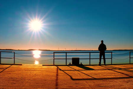 Man stand on wharf construction and looking at sea. Sunny clear blue sky, smooth water levelの写真素材