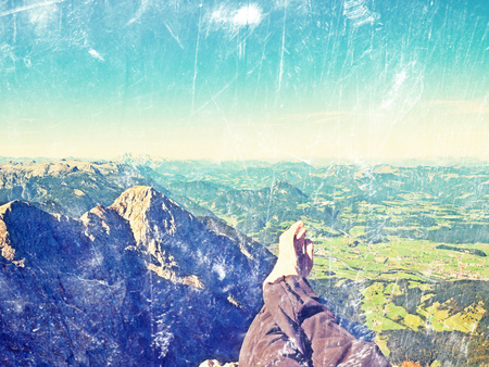 Film grain effect. The crossed legs take a  rest on tiring mountain trail. Sweaty male legs in dark trekking trousers relaxing on peak of mountain above valley.   Film scratch.の写真素材