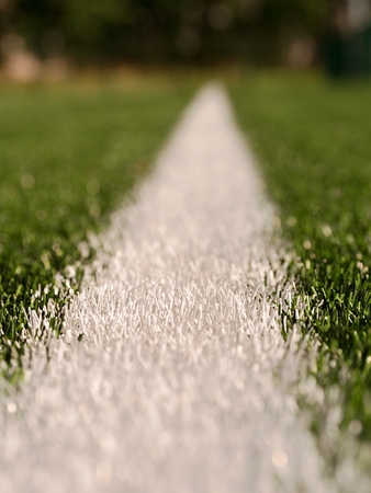 White line marks painted on artificial green turf background. Winter football playground with plastic grass. Play with Depth of Field.の写真素材
