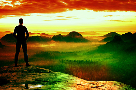 Film grain effect. Hiker is standing on the top of sandstone rock in rock empire park and watching over the misty and foggy morning valley to Sun. Beautiful moment the miracle of natureの写真素材