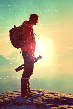 Film grain effect.  Silhouette of photographer overlooking a blanket of fog over valley to sunの写真素材