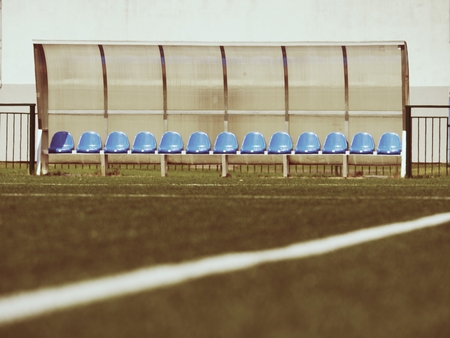 New blue plastic seats on outdoor stadium players bench, chairs with new paint below transparent plastic roof.  White line on football green turf playground.の写真素材