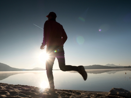 Man running on the beach against the backdrop of a beautiful sunset. Sand of mountain lake with deep foot trails.の写真素材